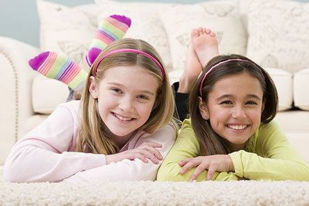 Girls smiling while laying on clean carpet.